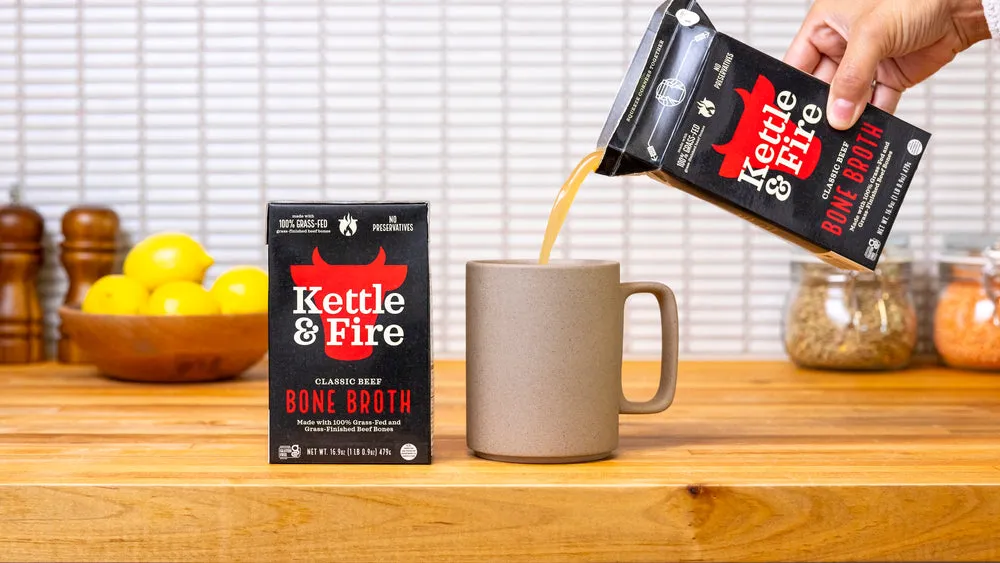 A carton of Kettle & Fire bone broth being poured into a mug on a kitchen counter